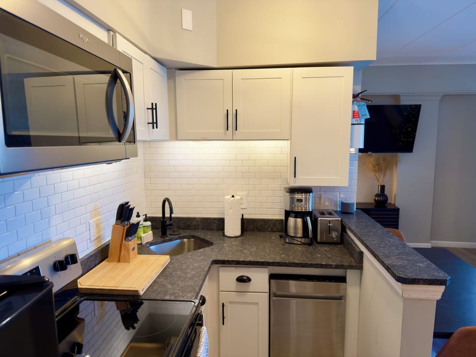 Modern full kitchen featuring stainless steel appliances, white cabinetry, sleek countertops and subway tile backsplash. Equipped with microwave, coffee maker and cooking essentials, perfect for preparing meals during your stay.