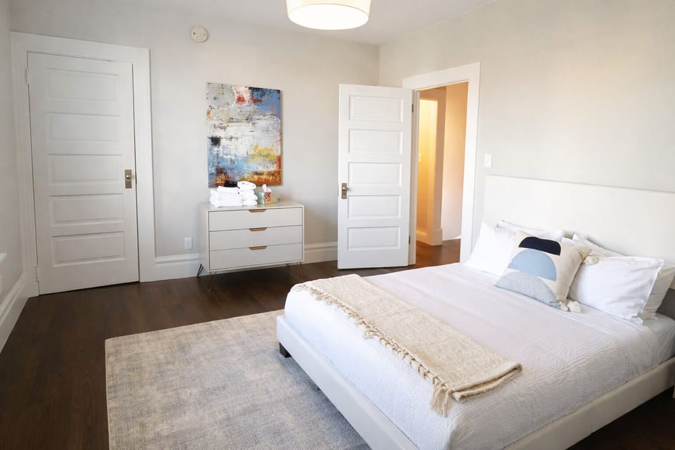 Retreat to the sun-drenched primary bedroom, featuring a comfortable king-size bed, designer art, and warm hardwood floors.