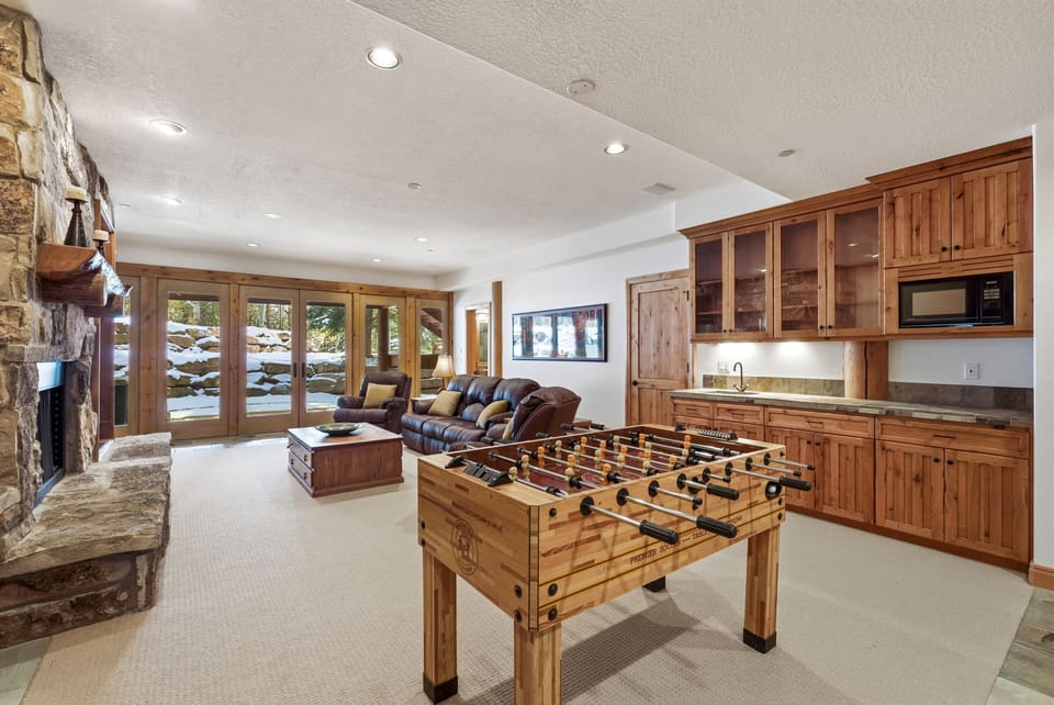 Lower-level entertainment room with foosball table, wood cabinetry, and full kitchen setup, perfect for group gatherings.