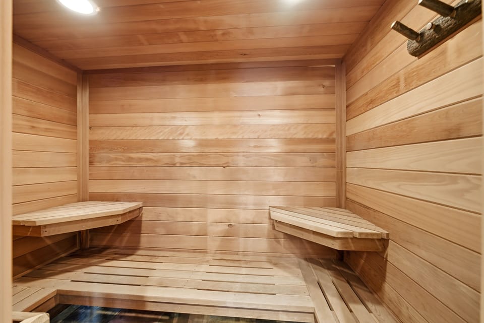Warm, wood-lined private sauna featuring upper and lower benches and soft lighting, offering a spa-like experience in-home.
