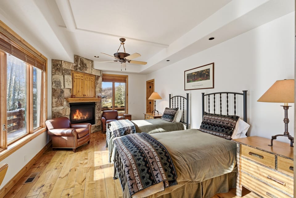 Rustic-style bedroom with corner fireplace, wood furniture, and sliding glass doors leading to a private balcony with mountain views.