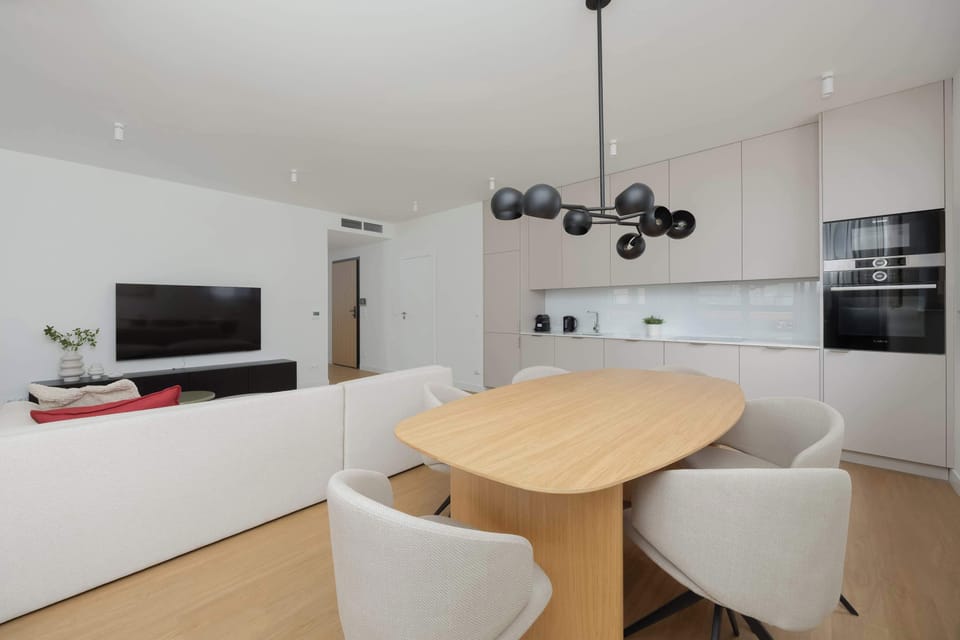 A spacious living room with a sofa, TV, and open layout. The light wooden floor enhances the modern and welcoming feel.