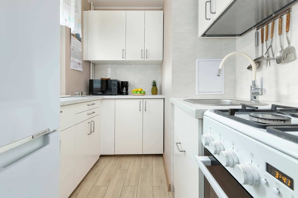 A compact white kitchen with modern cabinets, a gas stove, and a wooden floor.