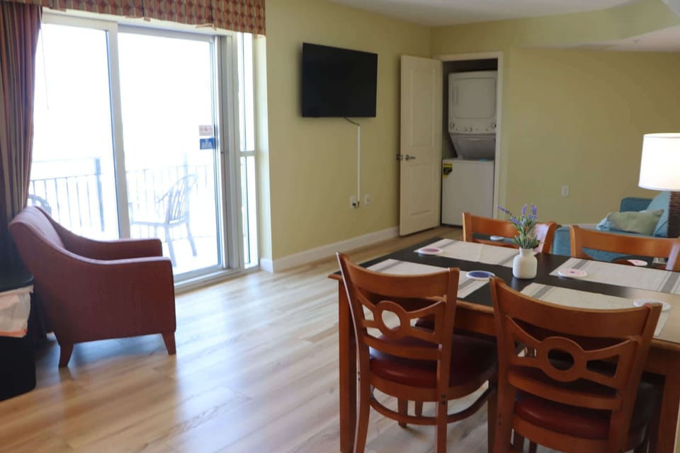 Comfortable dining and living area with balcony access, a wall-mounted TV, and in-unit laundry nearby — a convenient space to relax, dine, and enjoy your Myrtle Beach stay.