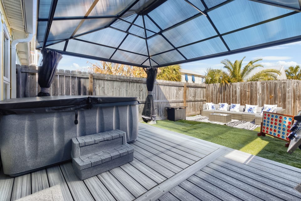 Cozy covered outdoor patio with string lights, a private hot tub, and a gas gril