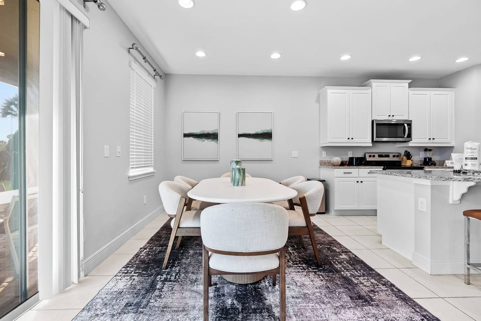 Enjoy meals or morning coffee in this bright dining area with a sleek white table and stylish upholstered chairs. The subtle grey rug adds warmth, and natural light flows beautifully through the large glass doors.