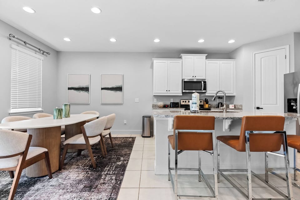 Enjoy a bright kitchen with sleek white cabinets and warm wooden accents. The inviting dining area, complete with a stylish rug, is ideal for meals and laughter, while modern bar stools offer a casual spot for your morning coffee.