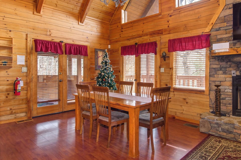 Gather around your rustic dining table where warm wood beams and stone fireplace create the perfect mountain cabin atmosphere for memorable meals.