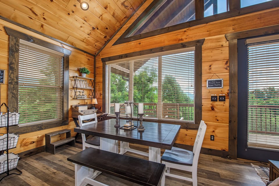 Picture yourself gathering around this farmhouse table in a warm, wood-lined cabin, where expansive windows frame lush forest views and vaulted ceilings add rustic charm.