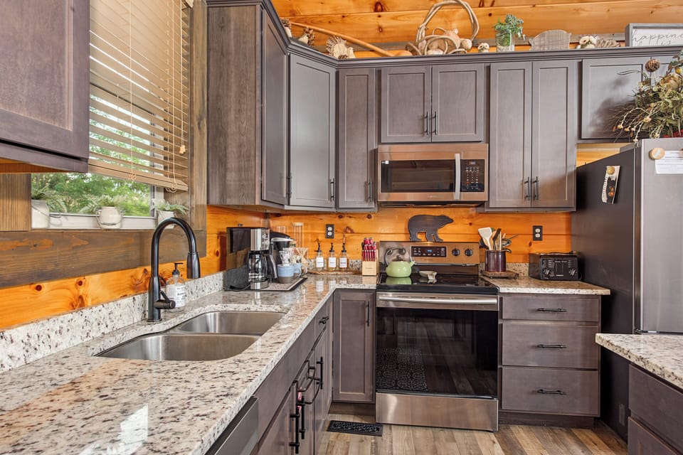 Your fully equipped kitchen features granite countertops, stainless steel appliances, and warm wood accents—perfect for preparing meals while soaking in the cozy cabin atmosphere.