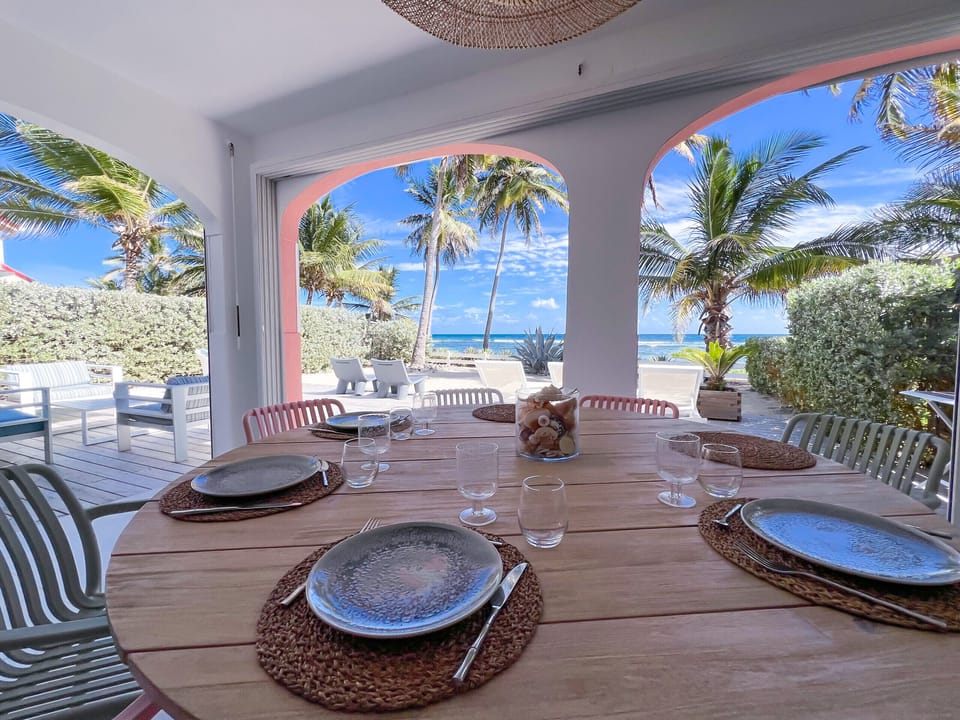 Stylish covered outdoor dining area featuring a large table, refined furniture and open views over the tropical garden, palm trees and the Caribbean Sea.