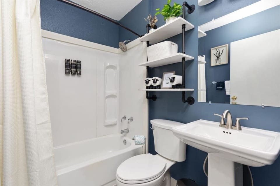Newly renovated and thoughtfully designed, this cozy bathroom features modern fixtures, a tub/shower combo, stylish open shelving, and convenient wall-mounted shampoo and soap dispensers. 