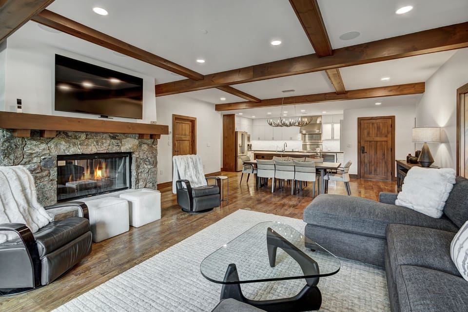 The heart of the condo is a stylish living area adorned with warm wood beams and a central fireplace, exuding a sophisticated mountain ambiance.