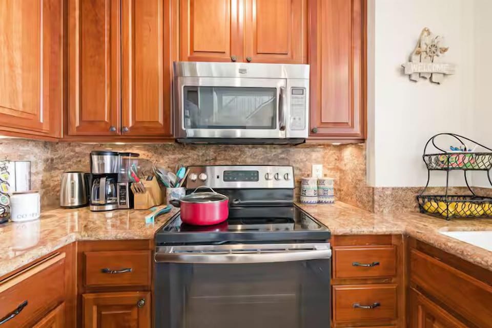 fully equipped kitchen with pots and pans, stove, oven, microwave, coffee maker, electric kettle, cooking utensils, dishes, silverware, and glasses.