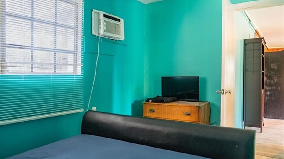 Bedroom with large bed, TV, window AC, and storage
