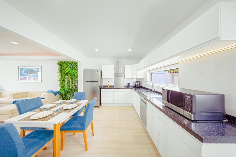 A sleek, modern chef’s kitchen awaits. Featuring crisp white cabinetry, quartz countertops, and high-end stainless-steel appliances, it’s perfect for cooking in style. Enjoy casual meals by the dining area overlooking the lush green wall.