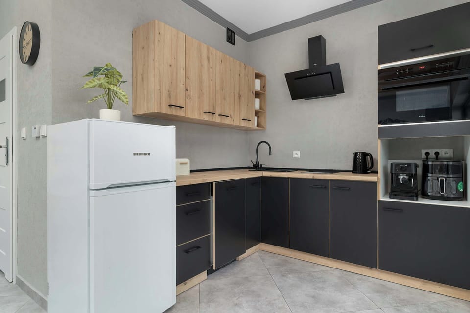 A kitchen with white and wood cabinetry, black countertops, and modern appliances. The design is practical with a contemporary touch.