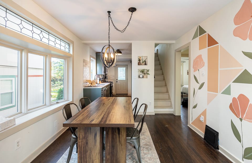 Bright and airy dining area with oversized windows and a rustic wood table—perfect for enjoying meals or gathering with friends before a short walk to the Plaza.