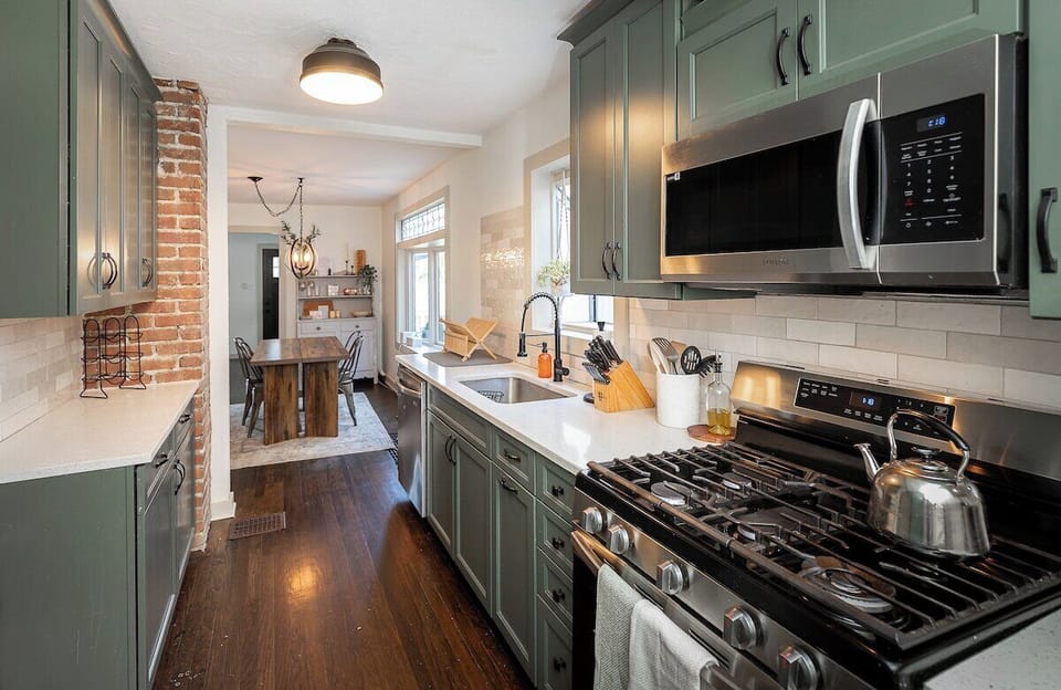 Stylish and fully equipped kitchen with sage cabinetry, exposed brick, and modern appliances—seamlessly connected to the dining room for effortless entertaining.