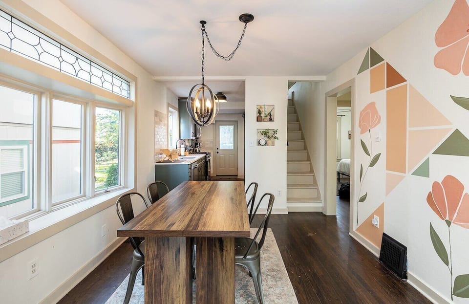 Bright and airy dining area with oversized windows and a rustic wood table—perfect for enjoying meals or gathering with friends before a short walk to the Plaza.