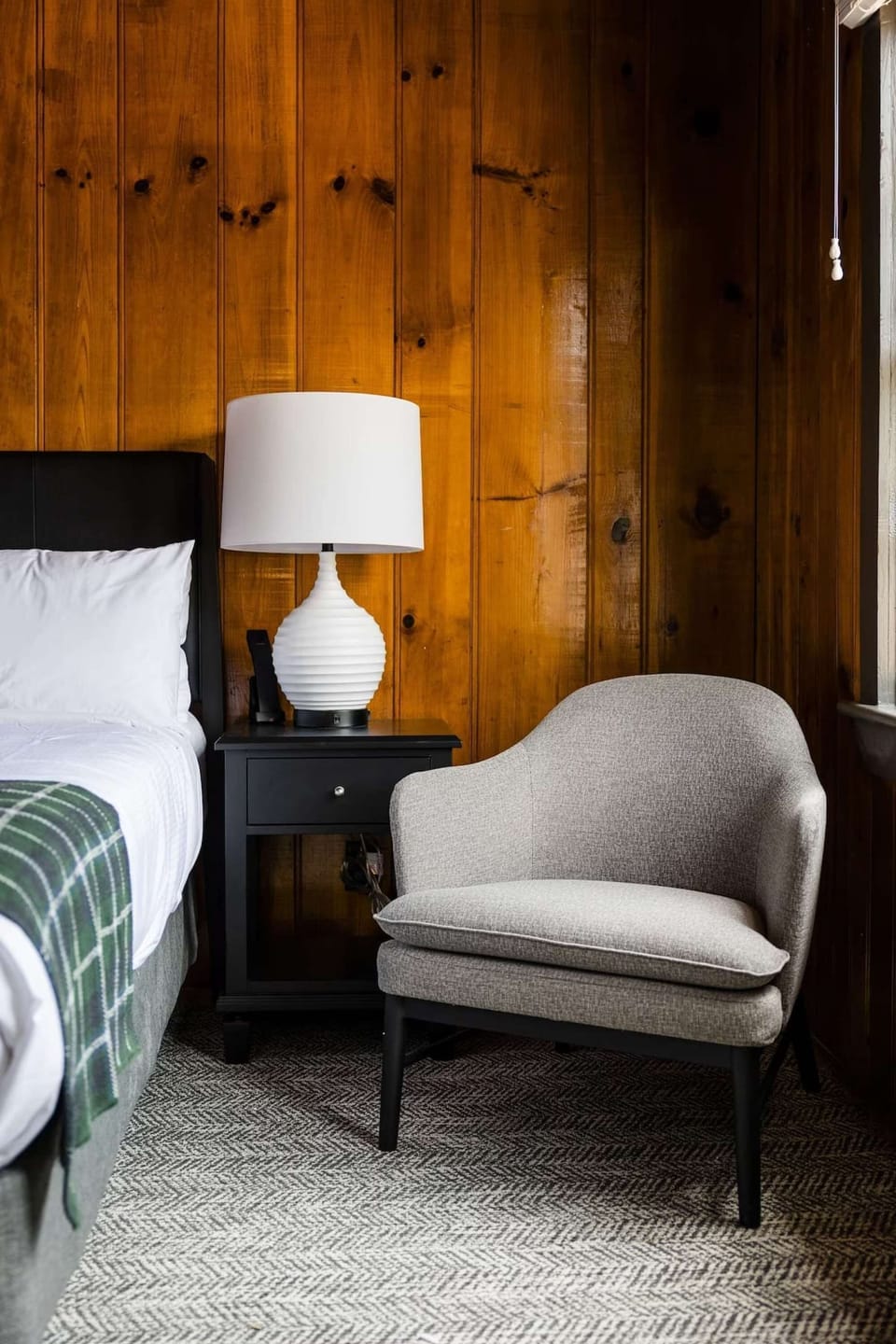 Soft chair and lamp beside the bed in a wood-paneled room