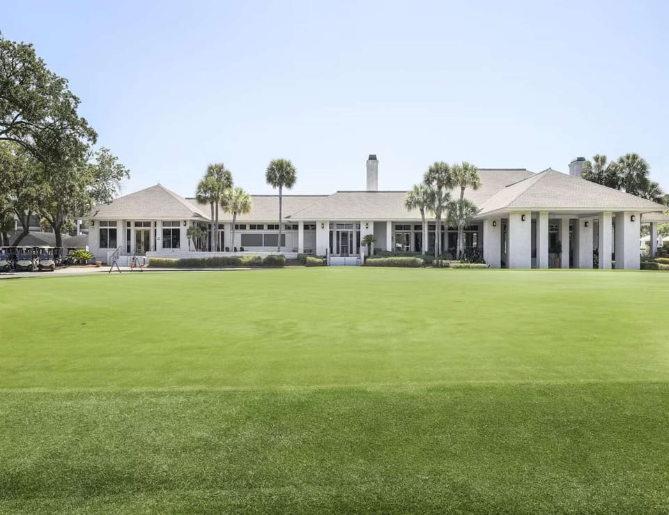 Large clubhouse with wide green lawn and palm trees in front