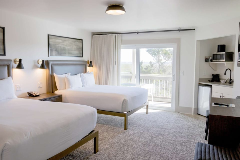 Two queen beds with marsh view balcony and kitchen space
