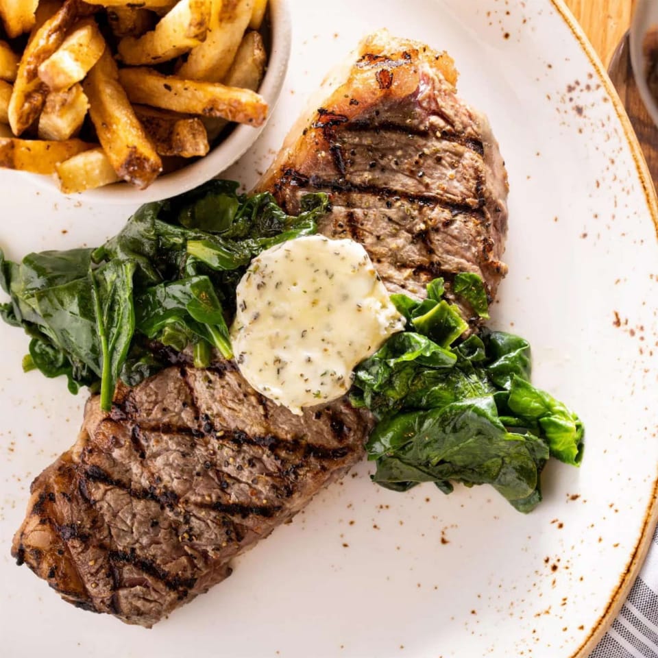 Grilled steak with sautéed spinach, herb butter, and golden fries
