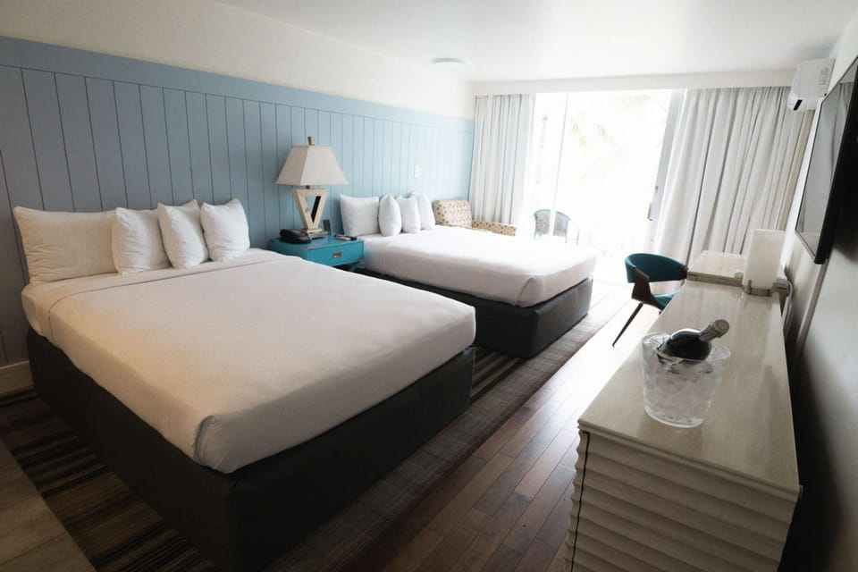 Spacious room with two queen beds and a balcony view of palm trees