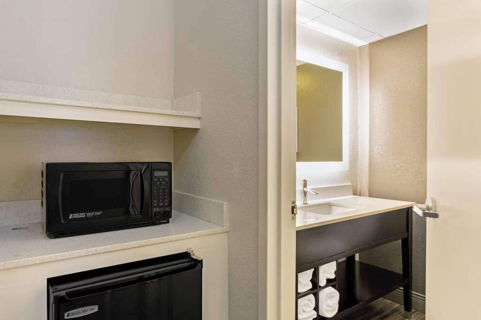 Microwave and fridge area next to bright bathroom vanity