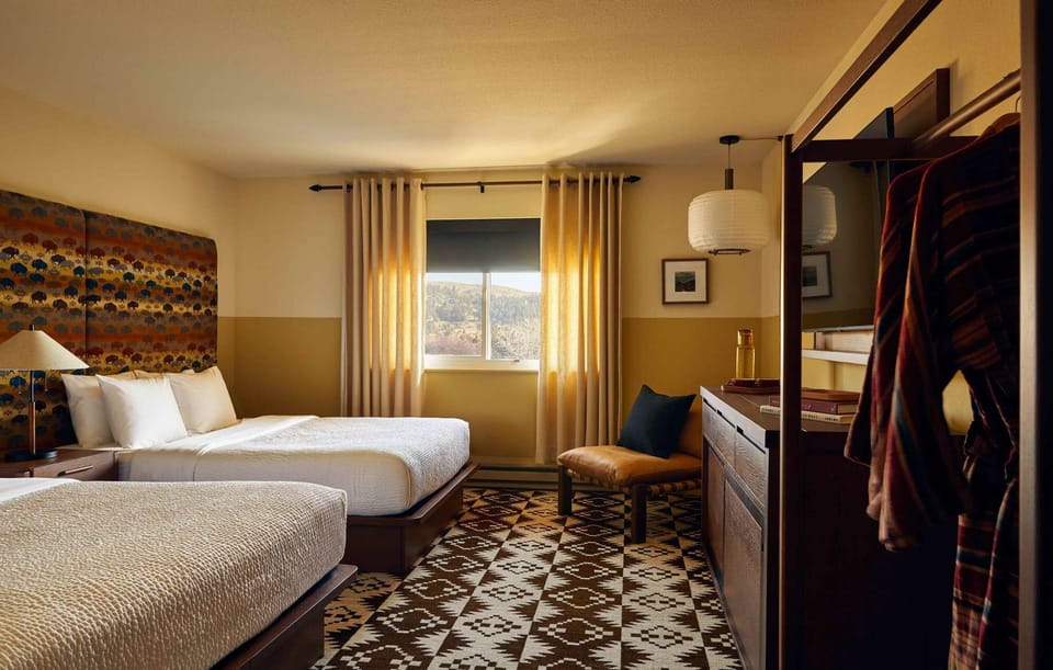 Two beds, window, bench, dresser, and patterned carpet