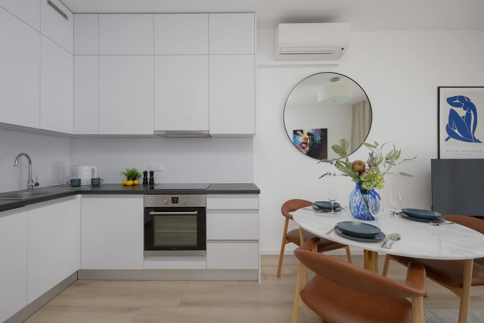 A clean and modern kitchenette with white cabinets, an oven, and a stove. The minimalist design emphasizes functionality and openness.