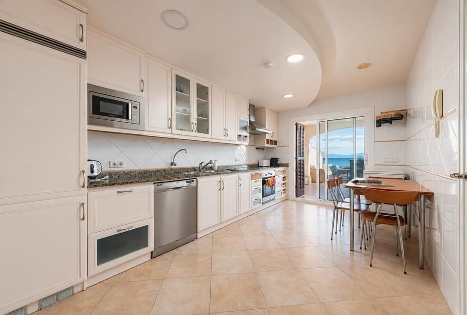 A spacious, white-cabinet kitchen featuring stainless steel appliances, a built-in microwave, and a small dining table setup.