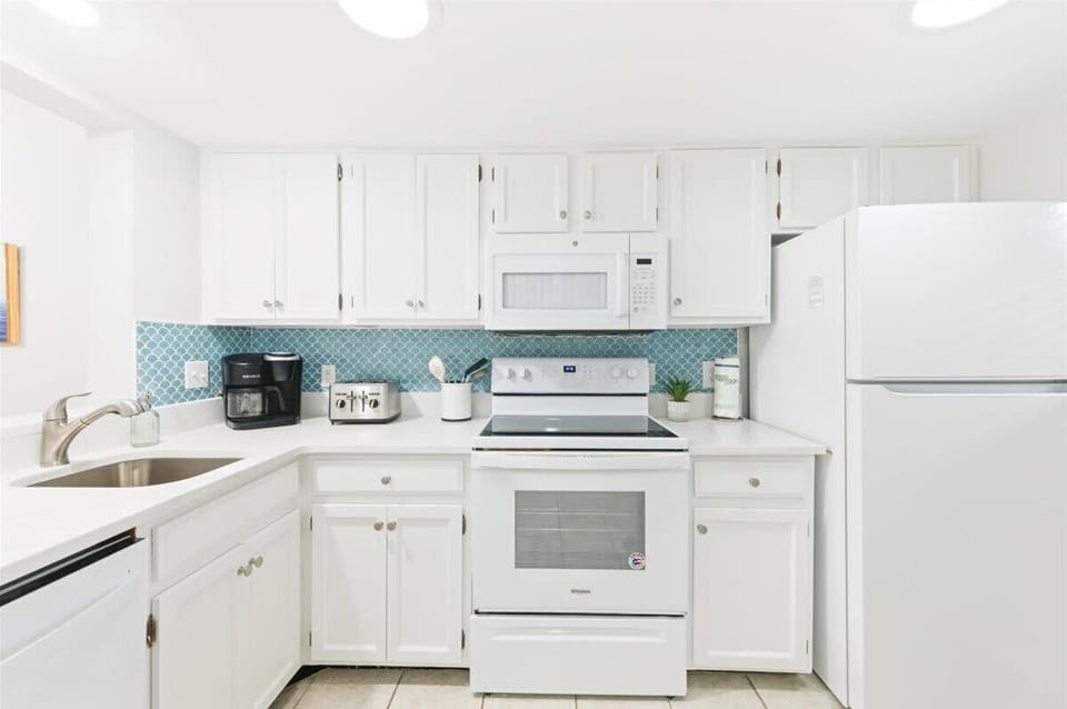 Bright, coastal kitchen with full-size appliances, coffee maker, and blue tile splash.