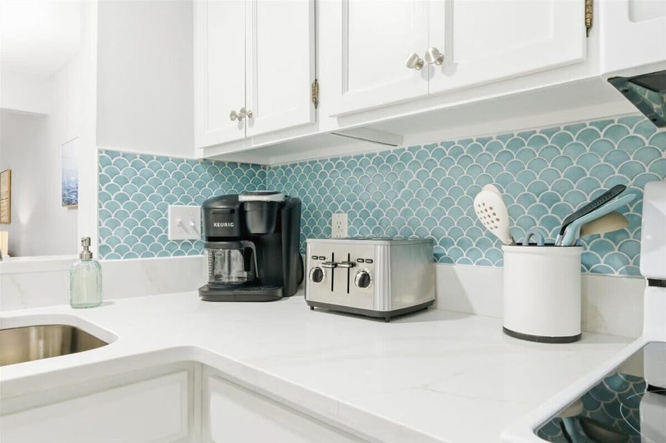 Bright, coastal kitchen with full-size appliances, coffee maker, and blue tile splash.