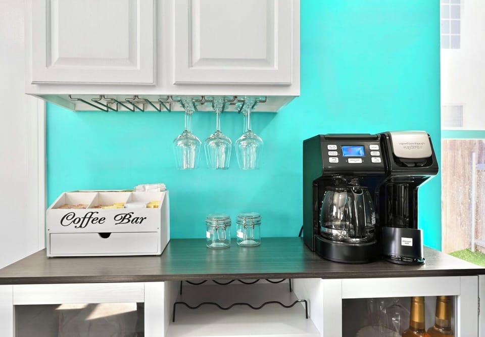 Bright coffee bar with dual brewer, supplies, and hanging stemware