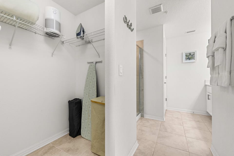 Bright bathroom area with open shelving, ironing board, and a tiled walk-in shower-minimalist and practical for a fuss-free stay.
