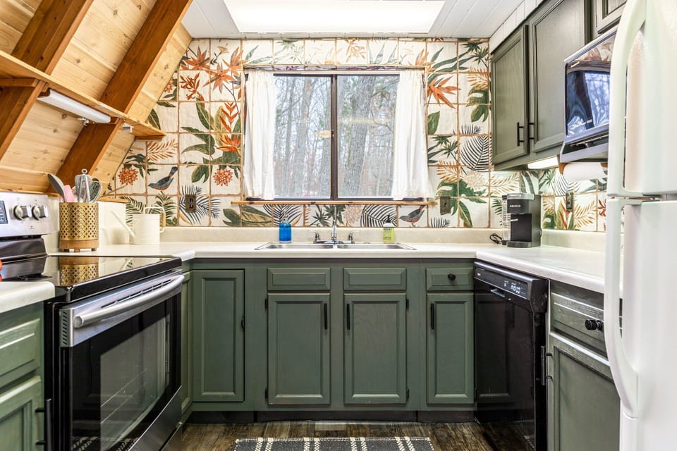 The compact kitchen features green cabinets, light counters, a range, dishwasher, refrigerator, sink, and single-serve coffee maker.