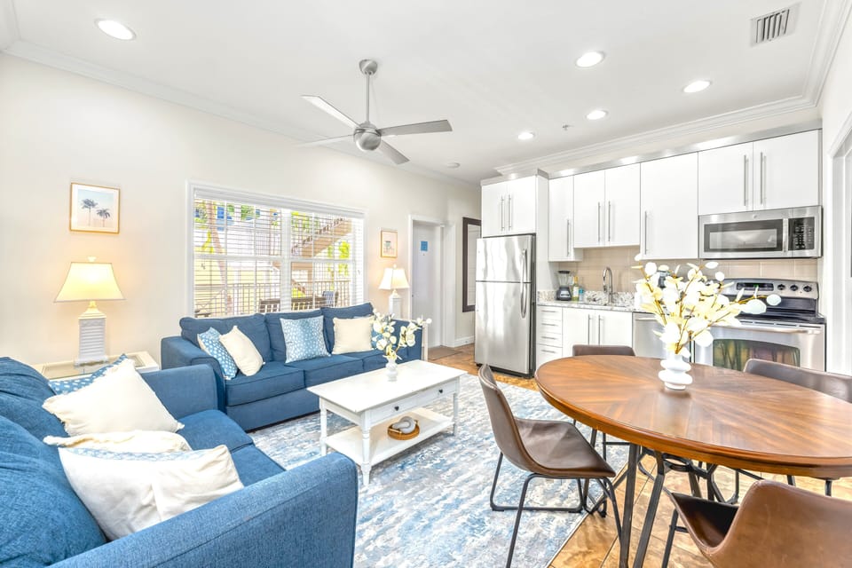 Living area open and sunny, opens to kitchen and dining.