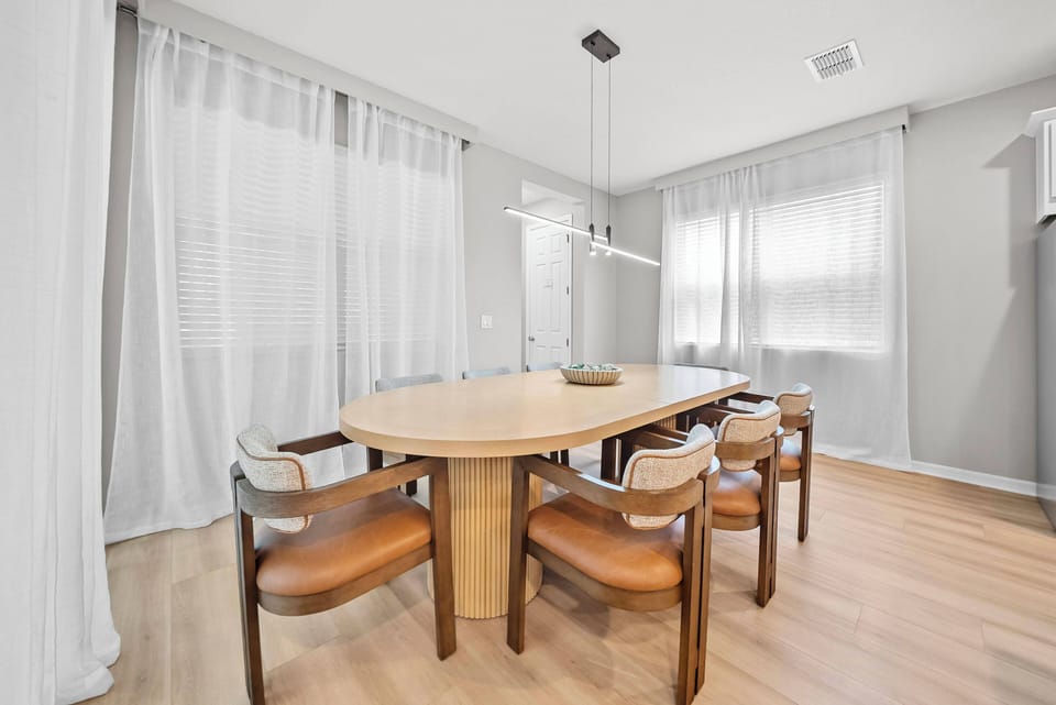 This bright dining area boasts a sleek oval table and stylish chairs, perfect for shared meals. Sunlight streams through sheer white curtains, creating a warm ambiance that encourages conversation and connection.