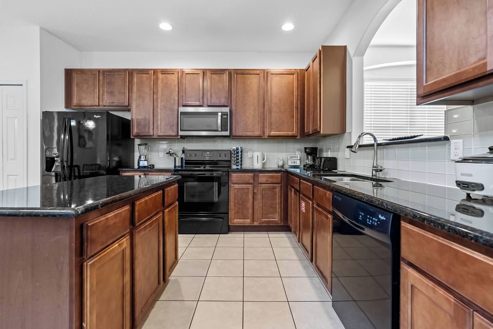 Enjoy cooking in this spacious kitchen with beautiful wooden cabinetry and sleek black appliances. The ample counter space and elegant tile flooring provide a functional and stylish setting for your culinary adventures.