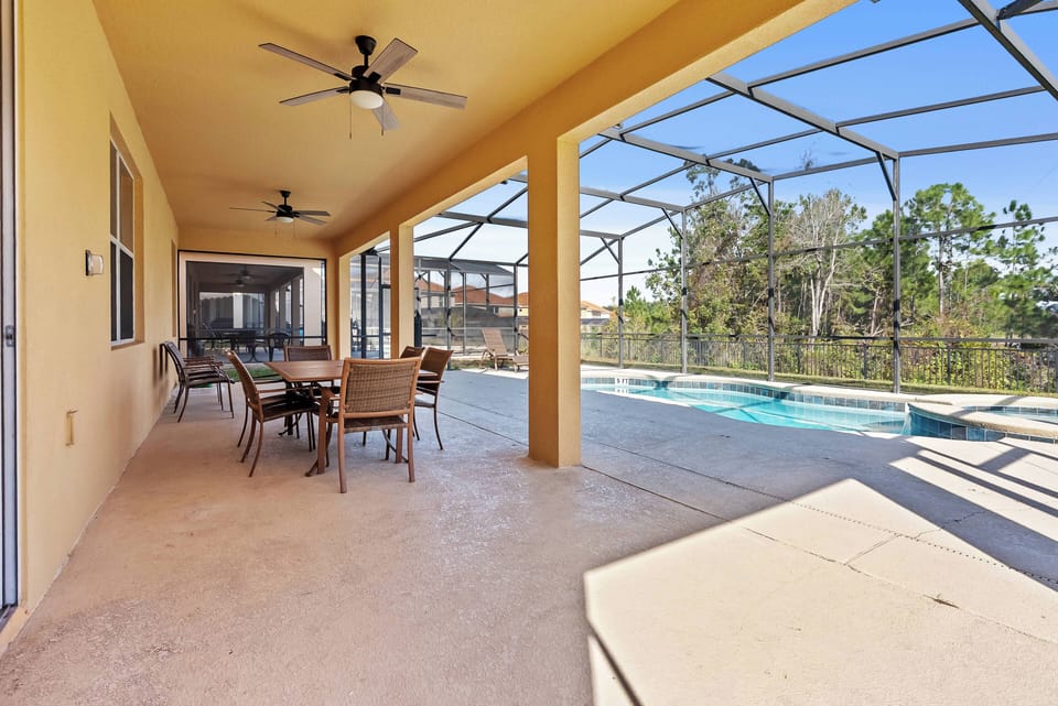 Step into a charming outdoor dining area, where a spacious table invites shared meals under the shade of a high ceiling. Large screened windows offer a seamless view of the shimmering pool, enhancing your relaxation experience.