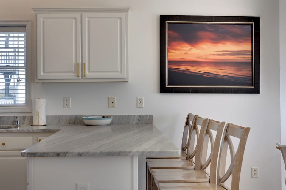 Bar seating for 4, and coastal art create a stylish spot for quick bites, cocktails, or sunset inspired dinners