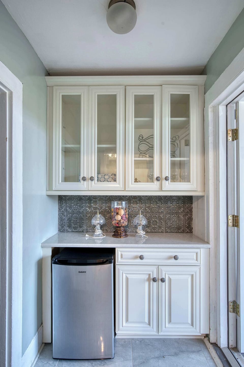 Chic built-in beverage nook with glass-front cabinets, elegant tile backsplash, and a sleek stainless mini fridge.