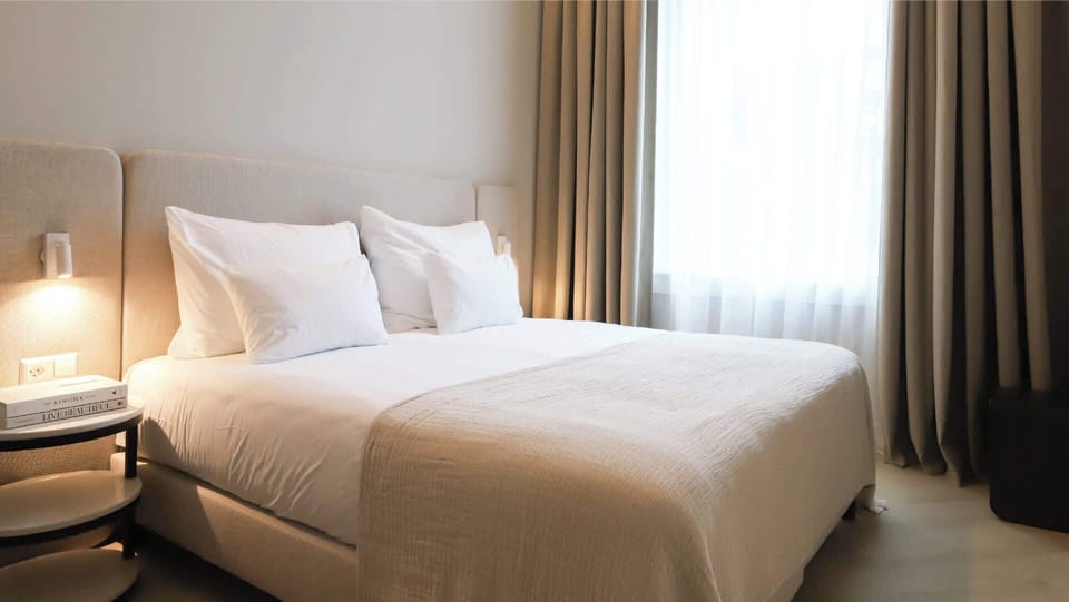 A calm and elegant bedroom with warm lighting, floor-to-ceiling curtains, and crisp white linens.