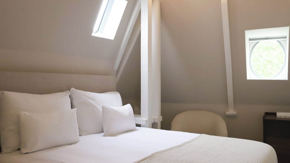 A tranquil attic-style bedroom with soft curves, clean lines, and a plush double bed under the beams.