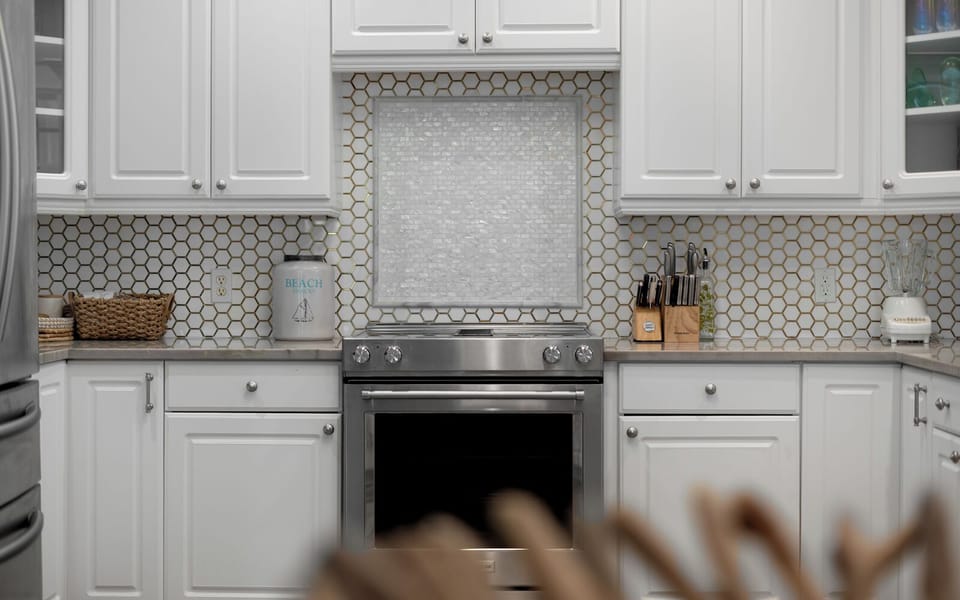 Your gourmet kitchen awaits with pristine white cabinets, stylish hexagonal backsplash, and premium stainless steel appliances ready for culinary adventures.