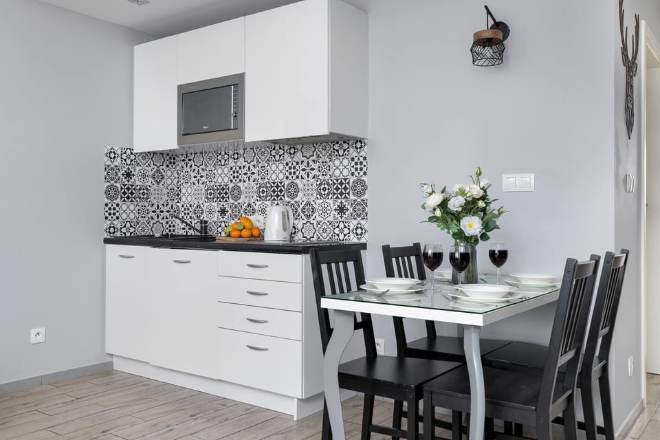 A kitchen and dining area with white cabinetry and a patterned backsplash. Black chairs contrast with the light interior. The space feels modern and functional.