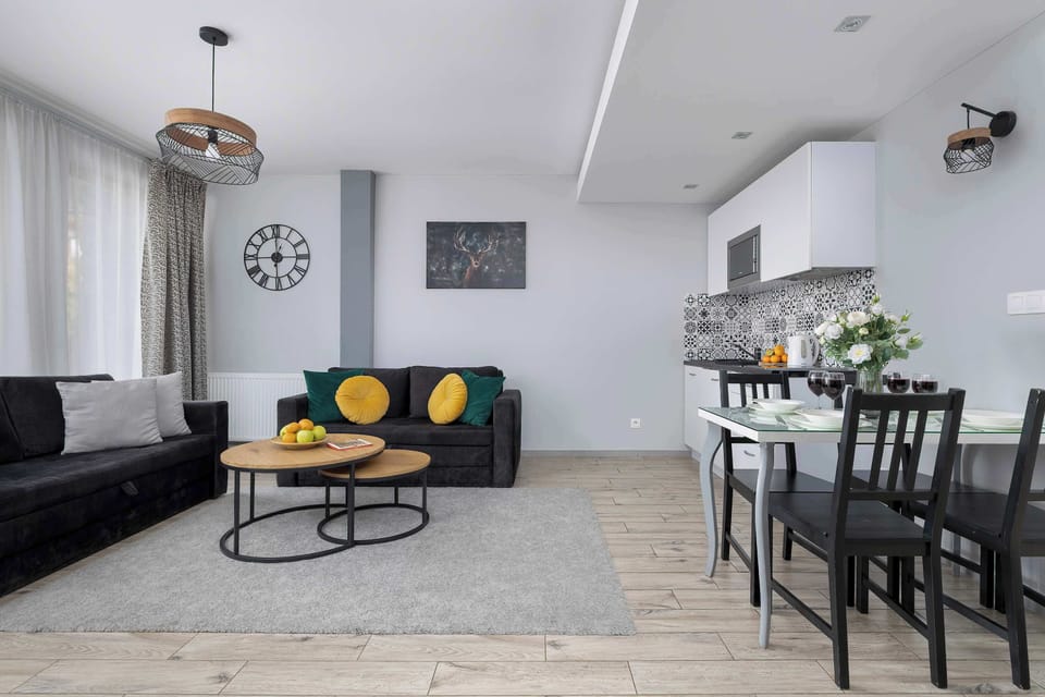 A combined living and dining area with a sofa, round coffee table, and dining table in the background. Pendant lighting hangs above the dining space. The layout is practical and modern.