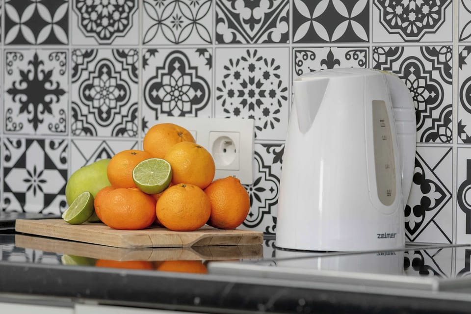 A close-up of oranges, a kettle, and a bowl placed on a patterned kitchen counter. The bold backsplash adds visual interest. The scene feels fresh and welcoming.